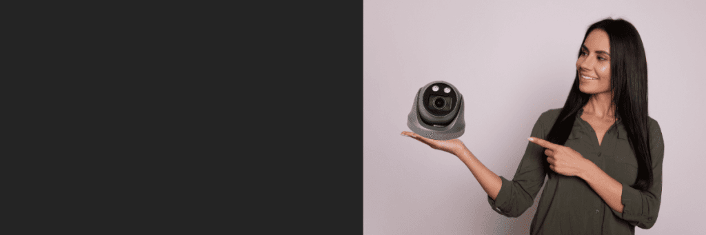 Frau hält eine schwarze Dome-Kamera in der Hand und zeigt darauf – moderne Präsentation von Sicherheitstechnik